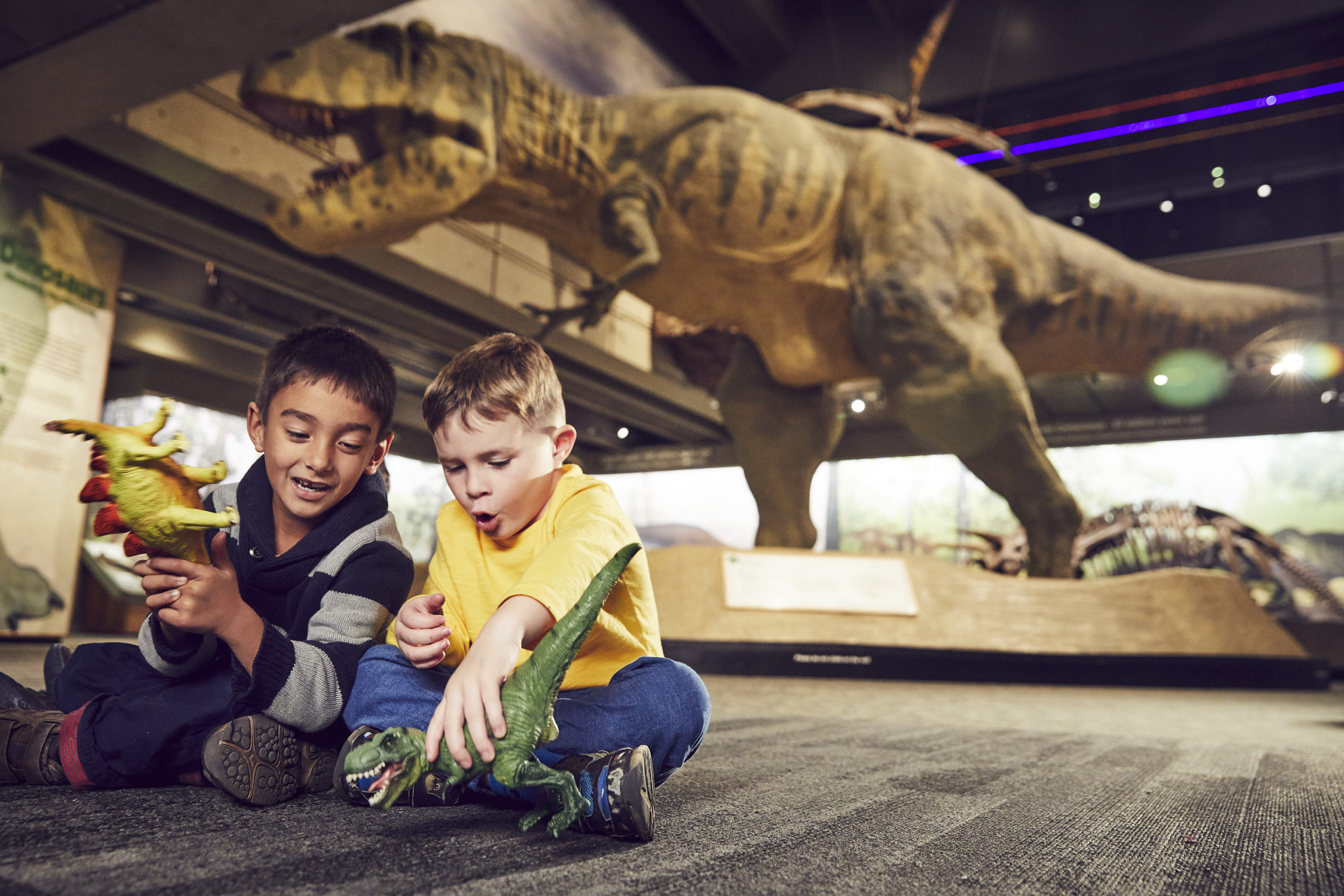 two boys play with dinosaur toys in a musuem